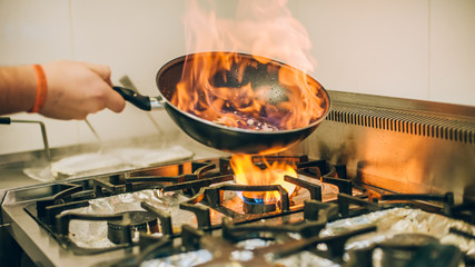 Le cuisinier de chef prépare le repas dans la poêle à frire de brûlure de feu de flamme
