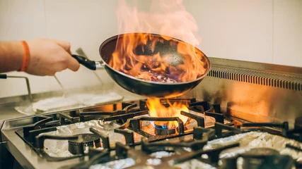 Photo sur Aluminium Cuisinier Le cuisinier de chef prépare le repas dans la poêle à frire de brûlure de feu de flamme