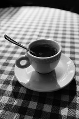 Lonely cup of coffee on cage stylized tablecloth. Black and white.