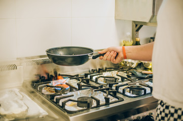 Chef cook prepares meal on frying pan in the kitchen