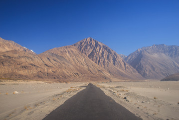 Straight road to mountains with blue sky background