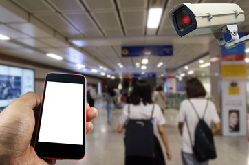 hand using mobile phone with blank screen and CCTV, security camera system operating at subway train station, internet, surveillance security and safety technology concept