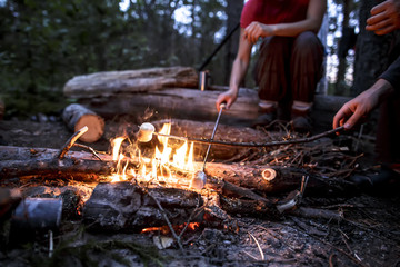 Two people are frying marshmeloo at the stake on a hike, on a warm summer evening.