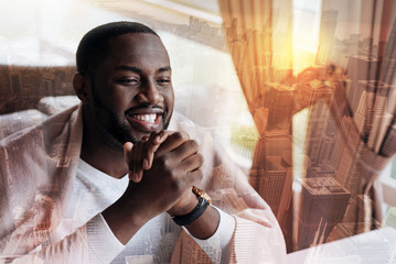 Happiness inside me. Attractive afro-american young man smiling and wearing a white shirt while sitting at the table