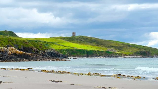 Dungloe, Ireland. Maghery beach in Dungloe, Ireland during the cloudy day. Ruins of a signaling tower at the background. Waves and sandy beach