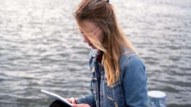 Young cute girl with tablet computer sitting close to the river 
