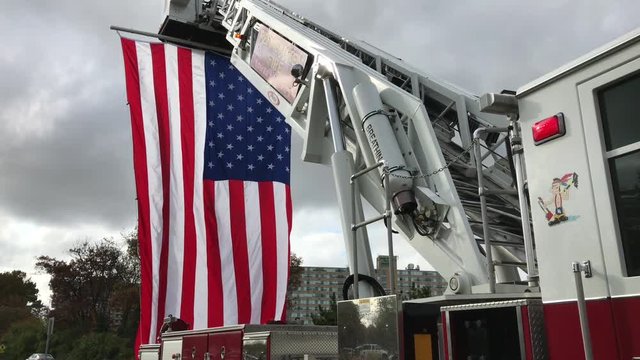 American flag blowing in breeze hanging from hook and ladder on fire truck
