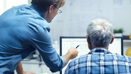 Two Senior Architectural Engineers Working With Building Plan on a Personal Computer. They Actively Discuss Various Plans and Schemes.