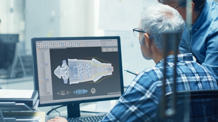Two Senior Aircraft Engineers Working With Turbine Blueprint on a Personal Computer. They Actively...