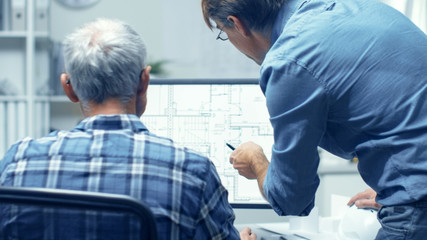 Two Senior Architectural Engineers Working With Building Plan on a Personal Computer. They Actively...