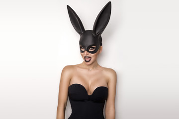 Sexy woman with large breasts wearing a black mask Easter bunny standing on a white background and...
