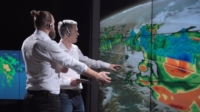 Two researchers in development center monitoring behavior of hurricane exploring live map changes. Elements of this image furnished by NASA.