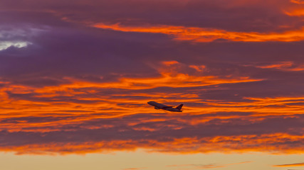 Aufnahme eines Flugzeuges im Flug vor tief rot ornage leuchtenden Wolken im Abendrot