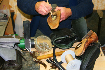 обувщик в мастерской, ремонтирует туфли.
