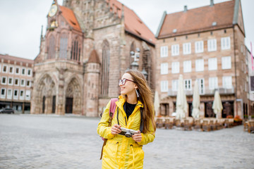 Young woman tourist in yellow raincoat standing on the main square of Nurnberg old town in Germany