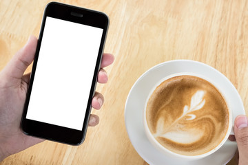 Fototapeta na wymiar A man hand holding smart phone with latte hot, coffee cup on wood desk in coffee shop. mobile with blank screen and can be add your texts or others.