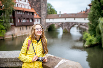 Young woman tourist in yellow raincoat with backpack standing on the old bridge over the Pegnitz river in Nurnberg city, Germany