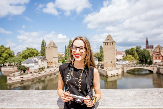 Portrait of a young woman tourist with photo camera on the beautiful landscape background with river and towers in the old town of Strassbourg city, France