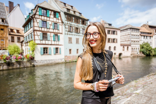 Young woman tourist standing with photo camera with beautiful old buildings and water chanal in Strasbourg city in France