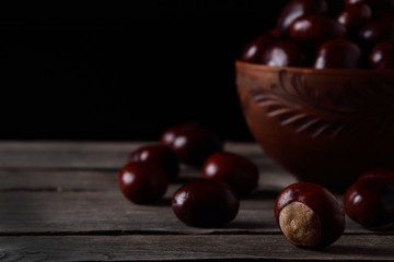  Fresh chestnuts in a bowl on an old wooden table. Group of chestnuts. Chestnuts - fruits horse chestnut - Aesculus hippocastanum. Dark background. Autumn background