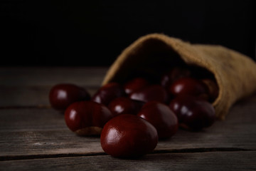  Chestnuts strewing from a bag on a wooden background in dark tones with a leaf with a very high color