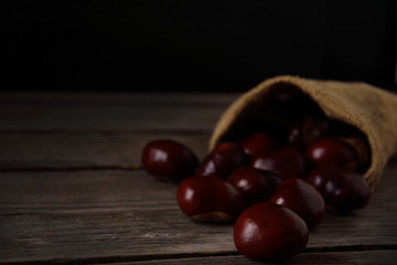  Chestnuts strewing from a bag on a wooden background in dark tones with a leaf with a very high color