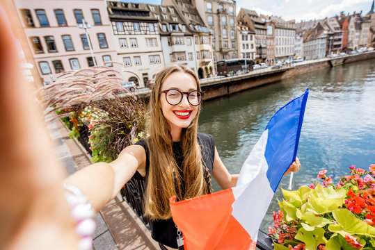 Young woman tourist making selfie photo with french flag on the old bridge over the water canal traveling in Strasbourg city, France