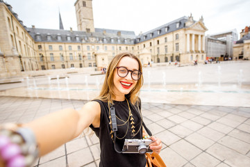 Young and happy woman tourist making selfie photo standing on the main sqaure in Dijon city, France