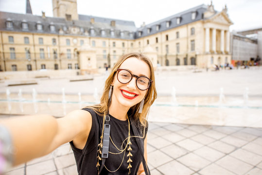 Young and happy woman tourist making selfie photo standing on the main sqaure in Dijon city, France