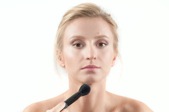 Beautiful woman applying dry cosmetic on the face using makeup brush.