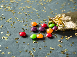 Colorful candies in the gold sack on gray background with stars