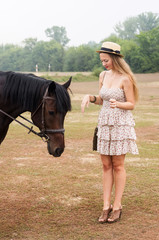 Blonde in a straw hat and a summer dress with a horse / The picture was taken in Russia, at the...