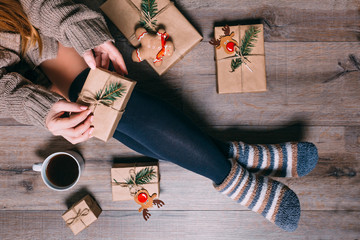 A woman sitting on the floor wrapping presents and drinking coffee at Christmas time