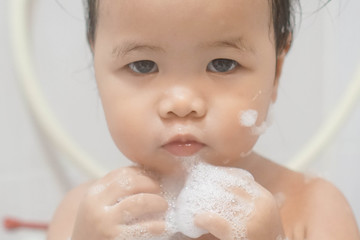 Little asian girl taking shower in bathroom, playing bath foam bubbles. Selective focus