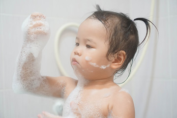 Little asian girl taking shower in bathroom, playing bath foam bubbles. Selective focus