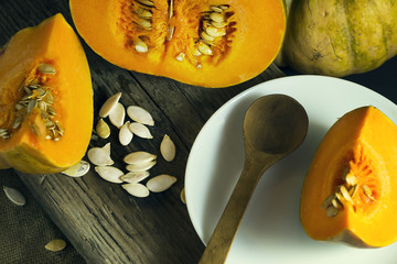 Sliced ripe pumpkin in a white plate with seeds and a wooden spoon. Harvest. Autumn.