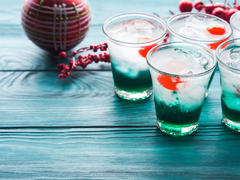 Christmas holiday party background with green alcohol drinks with cherry. Festive aperitif shots and ornaments on wooden dark table
