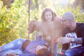 Beautiful gorgeous family of three playing in the park with their dog while lying on the grass. Animal lovers. Mother, father, daughter and their dog