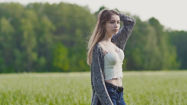 Young sexy and attractive girl posing at the camera on a background of green trees in beautiful purple sunset rays. Summer. The youth. Freedom.
