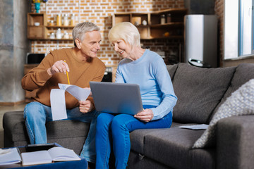 Family business. Positive delighted elderly couple sitting together and smiling while working on a...