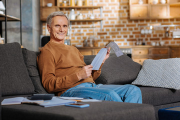 Fototapeta premium Financial issues. Cheerful happy positive man smiling and reading a document while dealing with financial issues