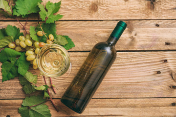 White wine glass and bottle and fresh grapes on wooden background, copy space