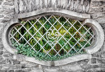 Old oval window with iron bars in stone wall