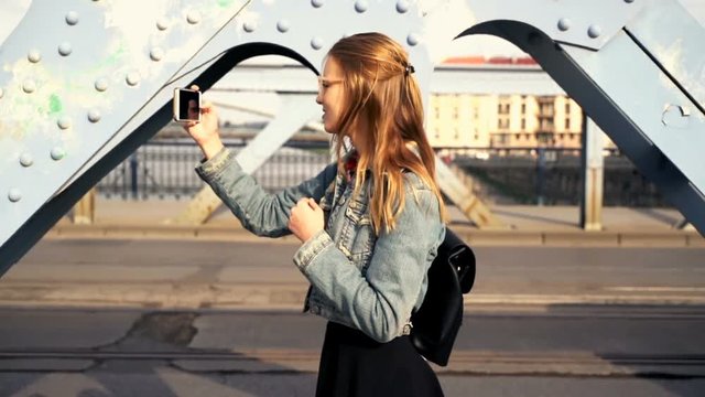 Woman taking photo with cellphone on the bridge in the city.
