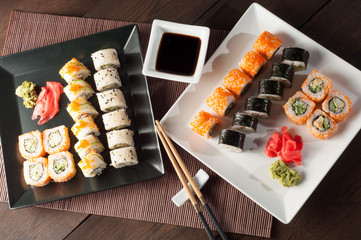 Sushi rolls on a black and white plate, on a wooden mat with chopsticks and soy sauce