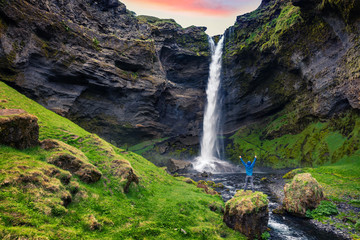Colorful morning view of Kvernufoss waterfall with man standing on the rock