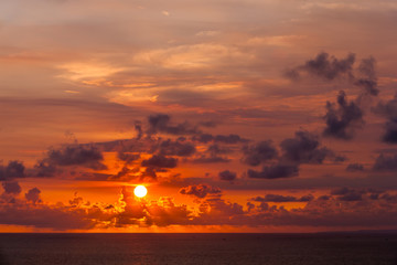 Bright colorful sun hides behind clouds of red color, goes beyond the horizon of the sea, the Indian Ocean. Amazing sunset from Uluwatu Temple, Bali, Indonesia.