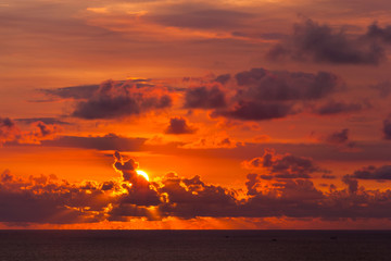 Bright colorful sun hides behind clouds of red color, goes beyond the horizon of the sea, the Indian Ocean. Colorful sunset from Uluwatu Temple, Bali, Indonesia.