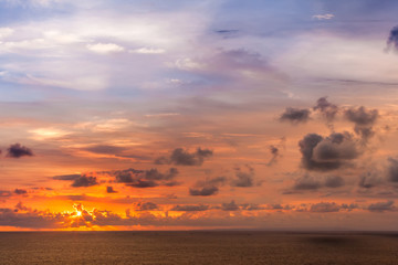 Fototapeta premium Bright colorful sun hides behind clouds of red color, goes beyond the horizon of the sea, the Indian Ocean. Beautiful sunset from Uluwatu Temple, Bali, Indonesia.