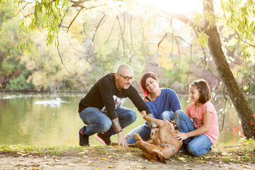 Family of father, mother and daughter on the riverside playing with their dog. Animal lovers